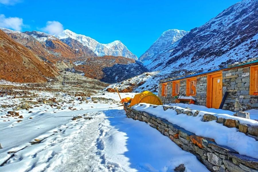 Stone teahouse in snow-covered valley surrounded by towering Himalayan mountains.