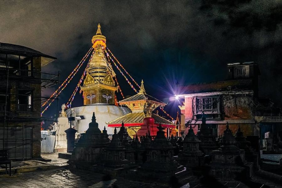 Swayambhunath Stupa illuminated at night with prayer flags.